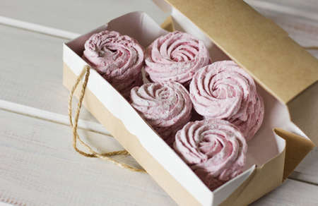 The homemade pink zephyr in a craft paper box on the white wooden backgroundの写真素材