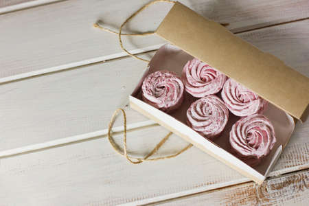 The homemade pink zephyr in a craft paper box on the white wooden backgroundの写真素材