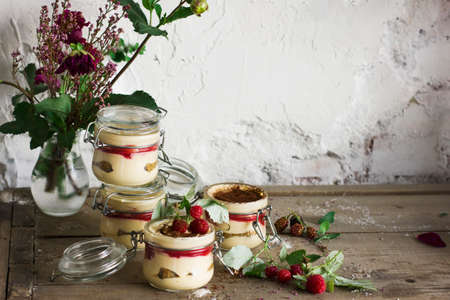 Homemade dessert tiramisu with raspberries in the glass jar on old wooden backgroundの写真素材