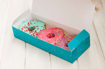 Colorful donuts in the cardboard box on the white wooden backgroundの写真素材