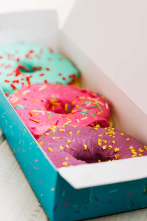 Colorful donuts in the cardboard box on the white wooden background