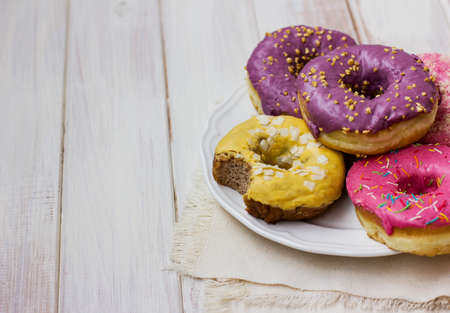 Fresh donuts with colorful glaze in the white plate on the wooden background. Copy space placeの写真素材