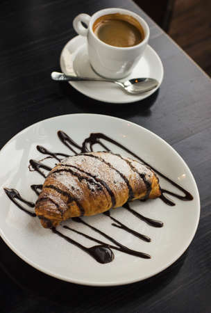 The big chocolate croissant and the Cup of espresso coffee on the black tableの写真素材