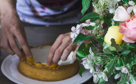 Homemade apricot pie on white plate with man hands. Beautiful rustic bouquetの写真素材