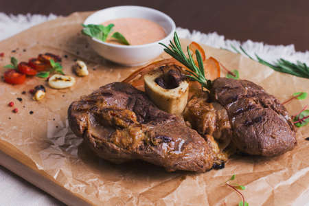 The large roasted piece of meat on the bone with sauce and spices on wooden boardの写真素材