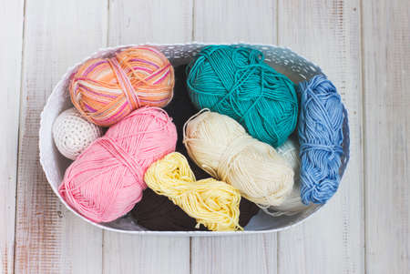 Multicolored cotton yarn in basket on white wooden background. View from top