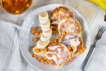Cottage cheese pancakes with banana slices and sea buckthorn berries. Healthy breakfast. View from topの写真素材