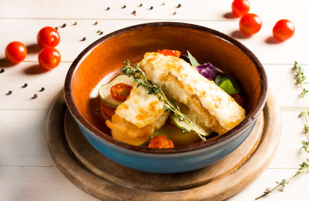 Baked chicken fish fillet with vegetables in a clay dish on a white wooden backgroundの写真素材