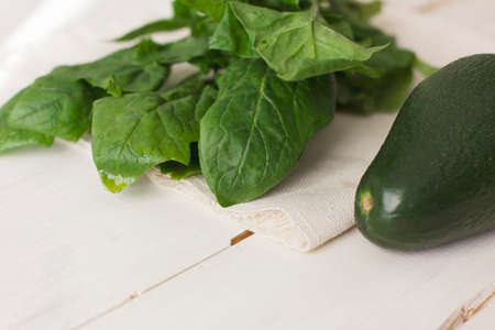 Bunch of fresh spinach and avocado on a white wooden backgroundの写真素材