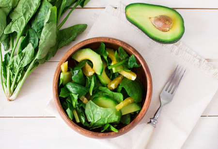Raw salad of spinach, avocado and orange in wooden plate on white backgroundの写真素材