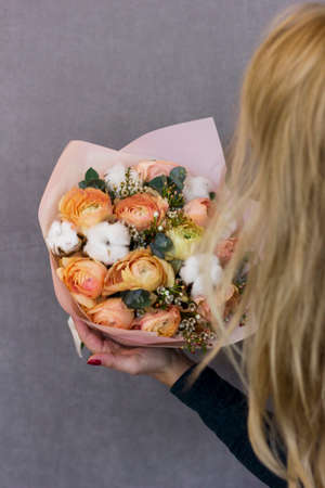 Beautiful blonde young woman holding in her hands delicate bouquet of flowers in rustic styleの写真素材