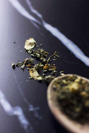 Herbal tea in a wooden spoon on a black marble backgroundの写真素材