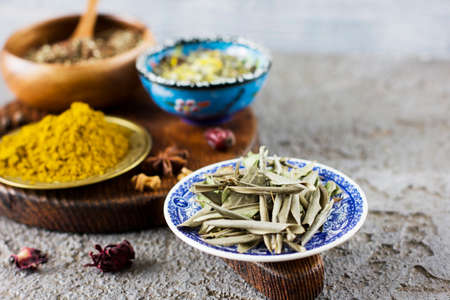 Dried olive leaves and dry spices in bowls on wooden Board on a concrete backgroundの写真素材