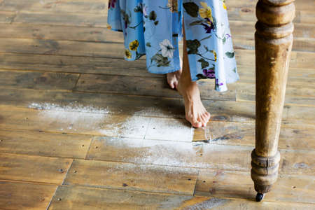 Female feet on the wooden floor of the kitchen with flourの写真素材