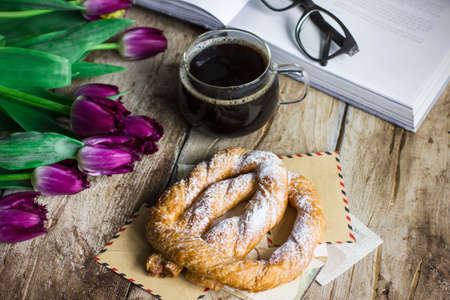 Still life with tulips, a book, coffee and a pretzel on the old wooden backgroundの写真素材