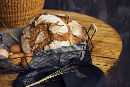 Loaf of rye bread in a basket with chicken eggs on the tableの写真素材