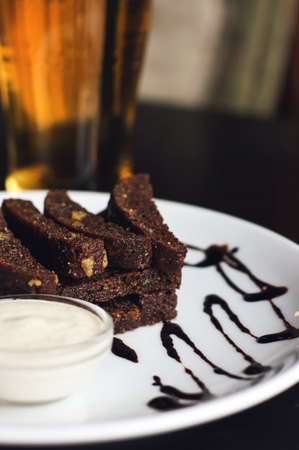 spicy rye crackers with garlic sauce mayonnaise snacks on white plate and beer on black table in bar