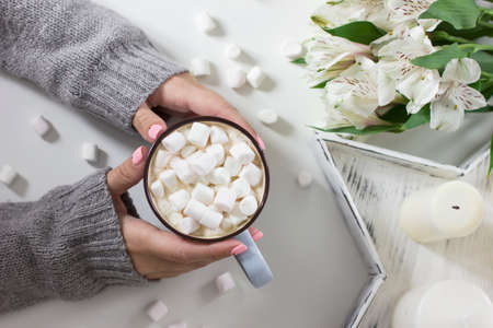Cocoa with marshmallows in female hands on white background flowers, candles, top viewの写真素材