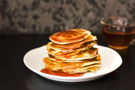 Homemade pancake poured syrup drops in white plate on dark background, closeup