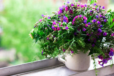 Wild forest meadow bouquet of cherry, lungwort, wild herbs in ceramic cup on window sill