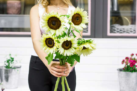 Young woman holding decorative light yellow sunflowers in the street near flower shopの写真素材