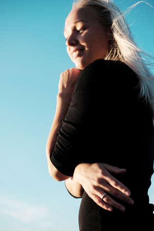 Lifestyle portrait of young blonde woman with smile in black dress against the skyの写真素材