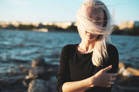 Lifestyle portrait of young blonde woman in windy day at sea, sunset lightの写真素材
