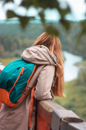 Girl traveler with red long hair standing on observation deck and looking at wild nature