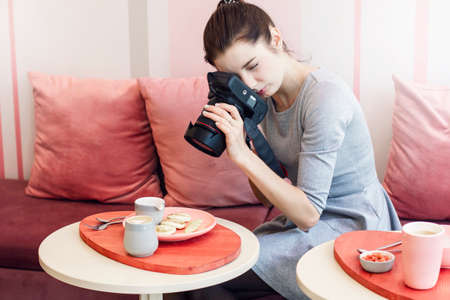 Young woman food photographer blogger shoots Breakfast in cafe, working processの写真素材