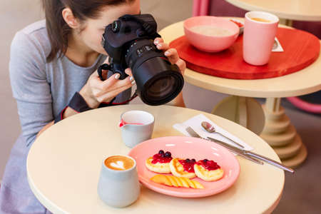 Young woman food photographer blogger shoots Breakfast in cafe, working processの写真素材