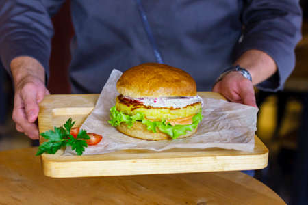Vegetarian Burger with potato cutlet, salad and sauce on wooden Board in male handsの写真素材