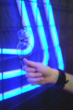 Glasses in metal frame reflect neon light in woman hands, blurred focusの写真素材