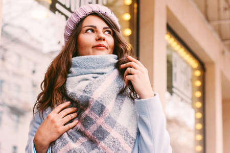 Young beautiful woman in coat and hat in late autumn or winter on city street enjoying life