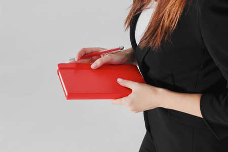 Woman business lady in black suit with red diary planner in hand on gray background isolatedの写真素材