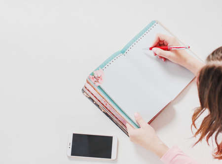 Still life with open planner notebook, women hands with pen and phone on gray background, top view