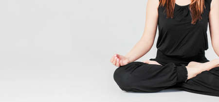 Young brunette slim woman in black sitting in Lotus position in yoga isolated on gray background, bannerの写真素材