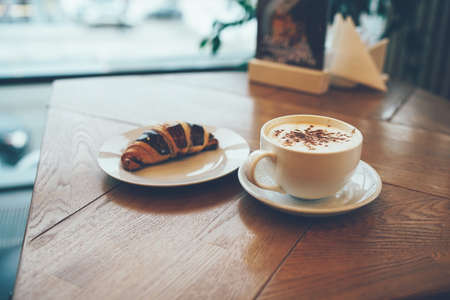 Breakfast with coffee and croissant on the table by the window in modern cafe, copy spaceの写真素材