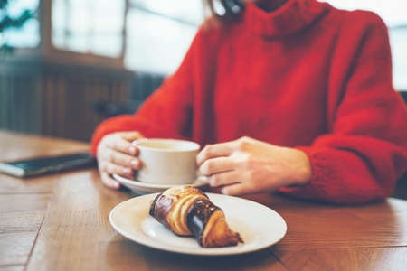 Coffee cappuccino in women's hands on the table, girl in cozy red sweaterの写真素材
