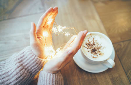 Young woman in cozy beige sweater holding garland heart of stars lights in hands