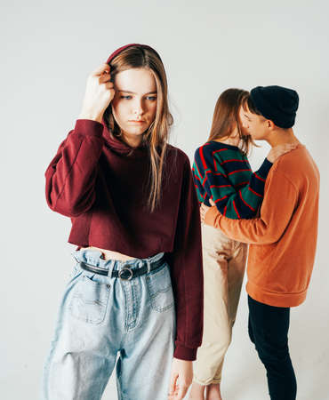 Sad young teen girl on background of loving couple, isolated. The concept of jealousy, loneliness