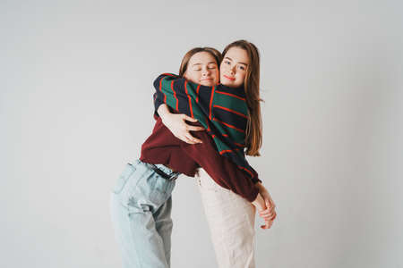 Two sisters twins beautiful girls hipsters in casual clothing on grey background isolated, concept love, friendship, soul matesの写真素材