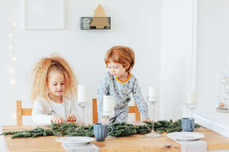 Cute sister and brother in pajamas at festive table, scandinavian interiorの写真素材