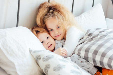 Little cute brother and sister in pajamas lie in bed, cozy morningの写真素材