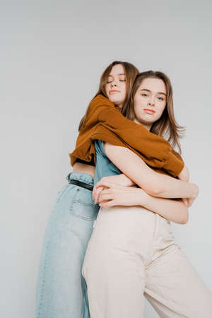 Two sisters twins beautiful girls hipsters in casual clothing on grey background isolated, concept love, friendship, soul matesの写真素材