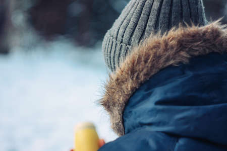 Man traveler forester hunter in the winter forest sitting on fallen tree with flask in his hands, close up, back viewの写真素材