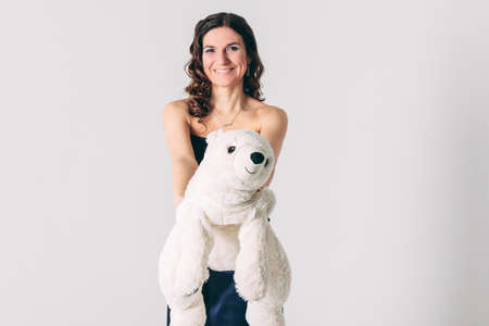 Young brunette woman in evening dress with polar bear toy on gray background isolated, concept of Valentine's dayの写真素材