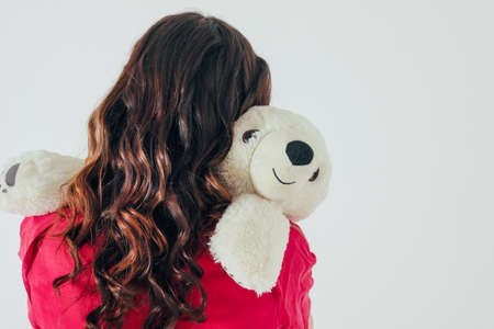 Polar bear toy hugs young curly brunette woman in bright pink dress on gray background isolated,...