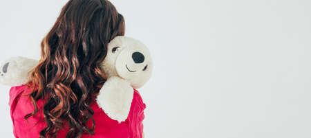 Polar bear toy hugs young curly brunette woman in bright pink dress on gray background isolated banner, concept of Valentine's dayの写真素材