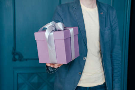 Gift box with gray silver ribbon in the hands of young attracrive man on blue backgroundの写真素材