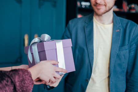 Woman get gift box with gray silver ribbon from young attracrive man on blue backgroundの写真素材